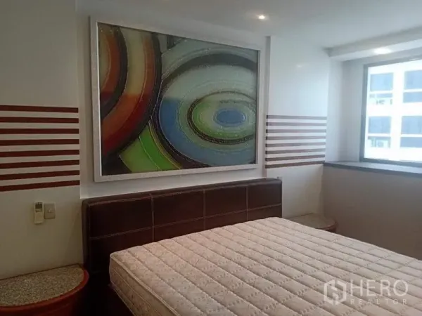 Condominium for rent in Khlong Toei, Bangkok - Bedroom with headboard, abstract wall art and a window for natural light.