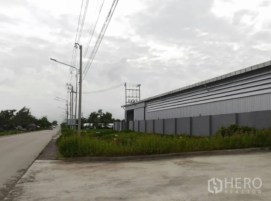 คลังสินค้า ให้เช่าในLam Luk Ka, Pathum Thani - ภาพด้านนอกโกดังสีเทาติดถนน กำแพงรั้วพร้อมเสาไฟ ทางเข้าคอนกรีตกว้าง