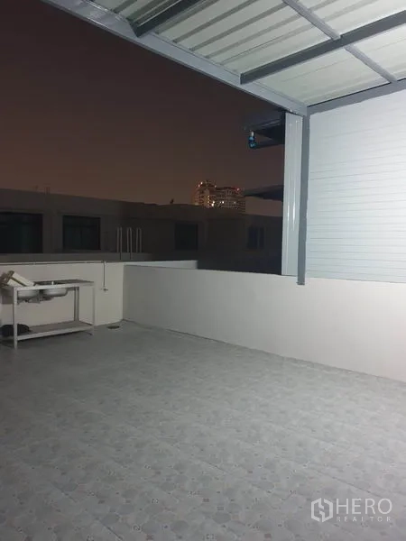 Home Office for rent in Wang Thonglang, Bangkok - Tiled rooftop terrace with partial metal roof and distant city view at night.