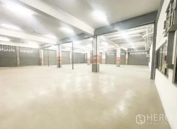 Warehouse for rent in Bang Phli, Samut Prakan - Spacious warehouse interior with concrete floor, columns, multiple roller shutter bays and bright LED lighting.