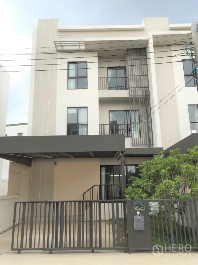 联排别墅 出租在Saphan Sung, Bangkok - 现代三层联排外立面，带大门的车棚、阳台与小树。