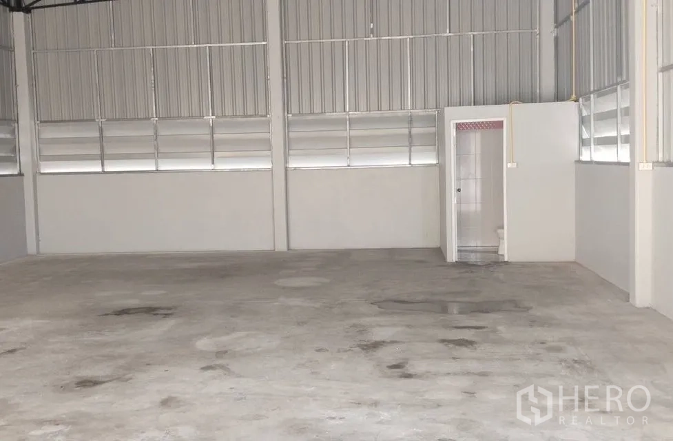 Warehouse for rent in Pak Kret, Nonthaburi - Open-plan warehouse interior with high ceiling, concrete floor, and an internal restroom.