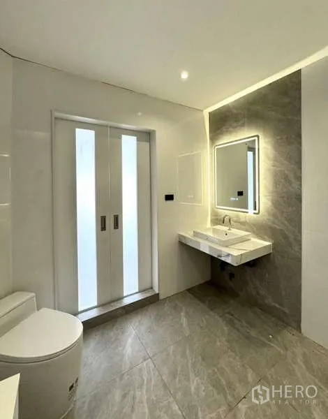 Townhouse for rent or sale in Prawet, Bangkok - Bright bathroom with backlit mirror, floating vanity, and frosted sliding doors.