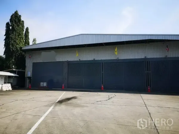 Warehouse for rent in Pak Kret, Nonthaburi - Front exterior of a metal-clad warehouse with multiple large doors and a wide concrete yard for truck access.