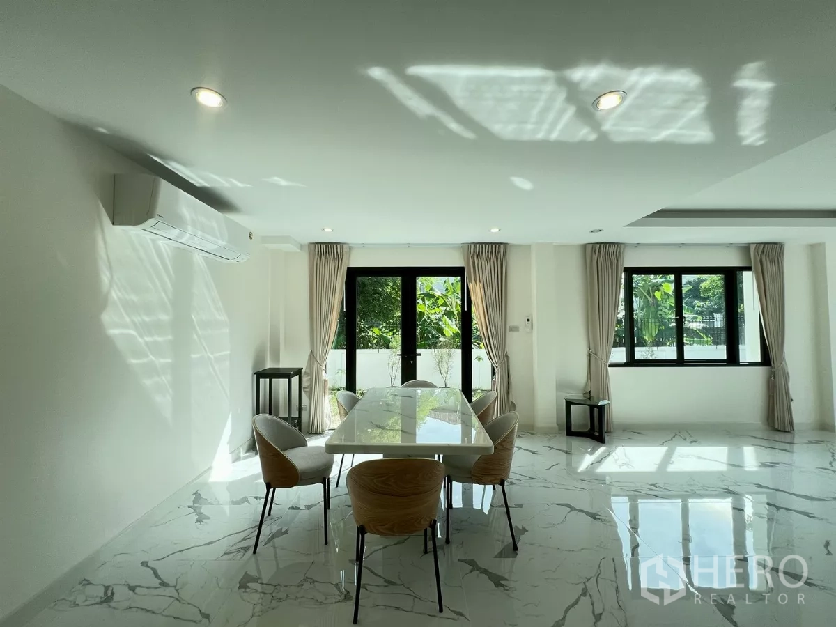 Detached House for rent in Suan Luang, Bangkok - Sunlit dining space overlooking greenery through black-framed windows.