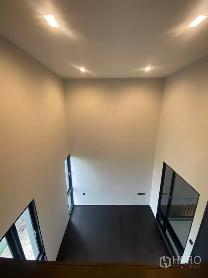 Townhouse for rent in Huai Khwang, Bangkok - View from the mezzanine into a lofty room with dark floors and tall windows.
