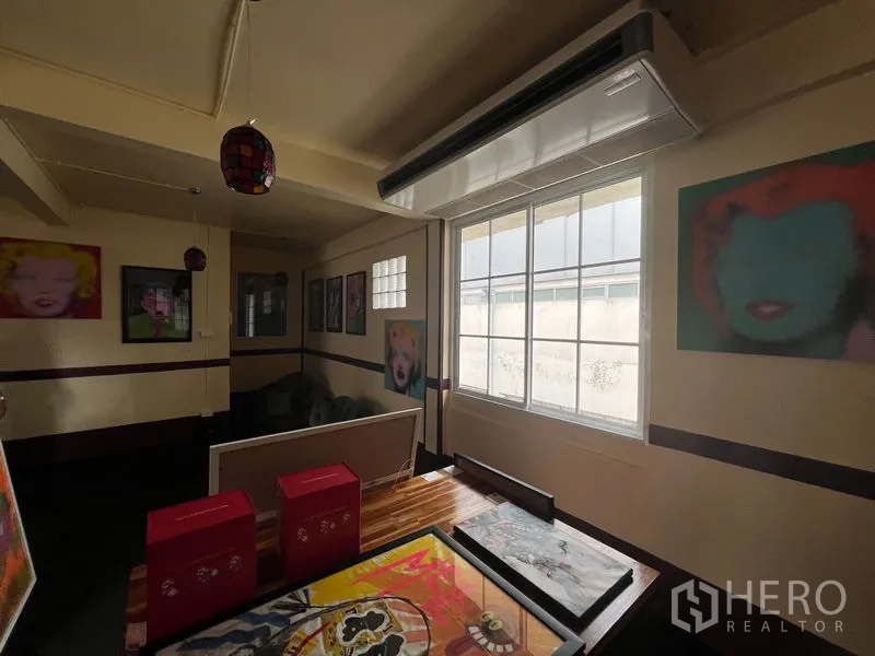 Shophouse for rent in Khlong Toei, Bangkok - Corner room with large window, wall-mounted AC and framed pop art.