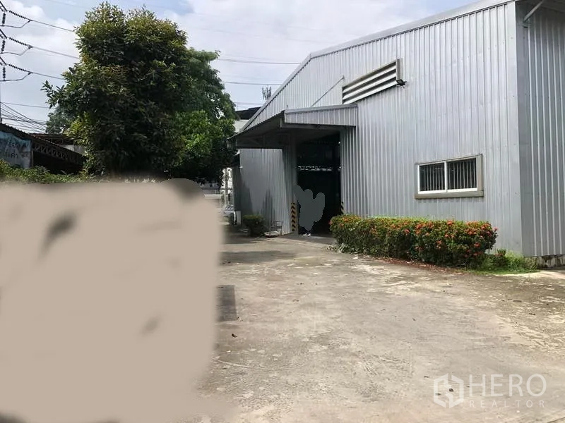 Warehouse for rent in Pak Kret, Nonthaburi - Front facade of warehouse with canopy entry, metal cladding, small windows and wide concrete yard.