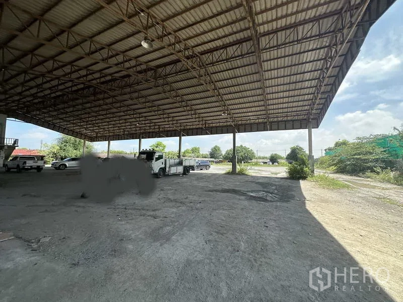 Factory for rent in Phra Nakhon Si Ayutthaya - Open-sided shed looking out to a spacious yard with trucks and parking under a high roof.