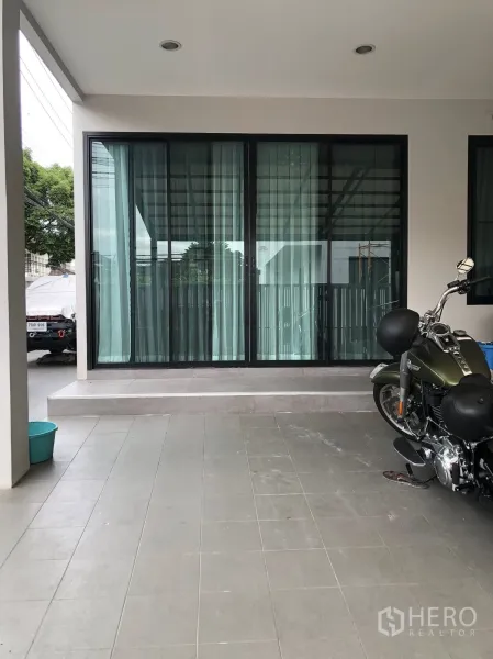 Townhouse for sale in Phra Khanong, Bangkok - Covered carport and front terrace with tiled floor and wide sliding glass doors.