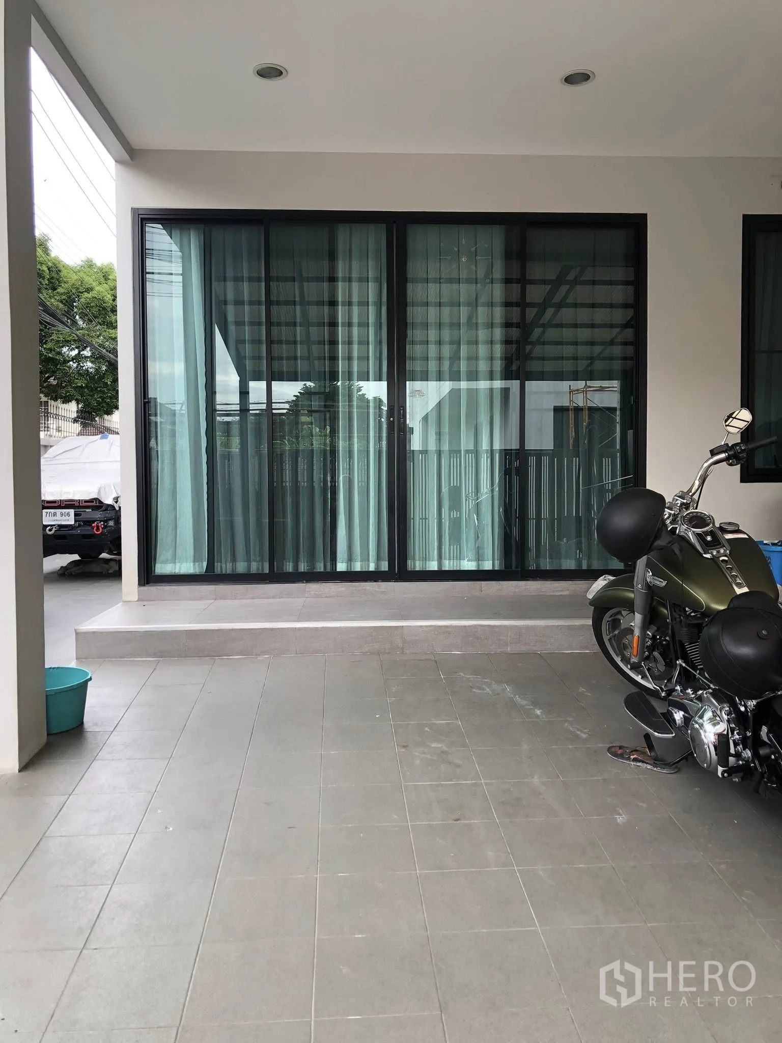 Townhouse for sale in Phra Khanong, Bangkok - Covered carport and front terrace with tiled floor and wide sliding glass doors.