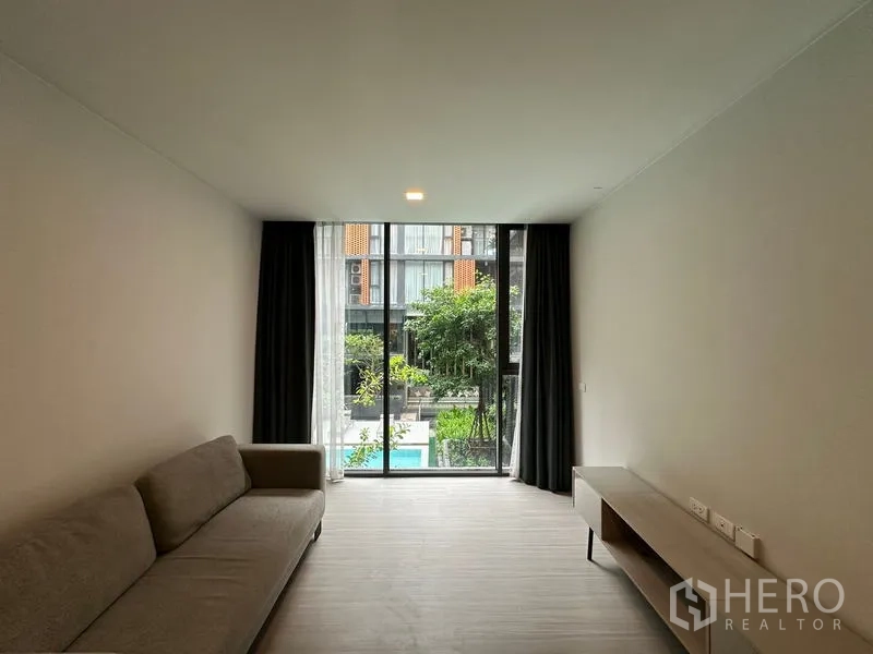 Condominium for rent in Khlong Toei, Bangkok - Bright living room in a Khlong Toei condo with floor-to-ceiling windows opening to garden and pool views.