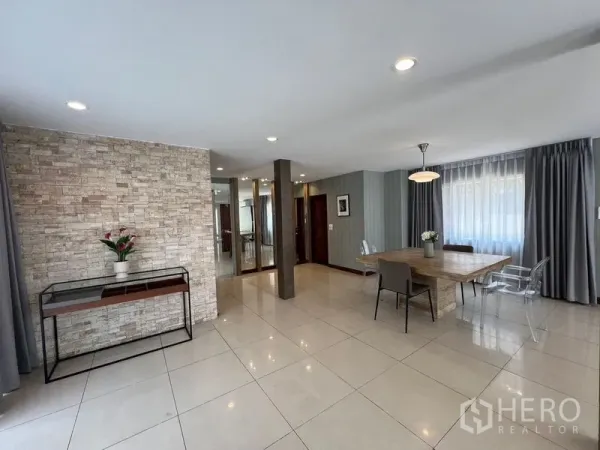 Detached House for sale in Mueang Pathum Thani, Pathum Thani - Bright dining and living area with stone feature wall, large wooden table and full curtains.