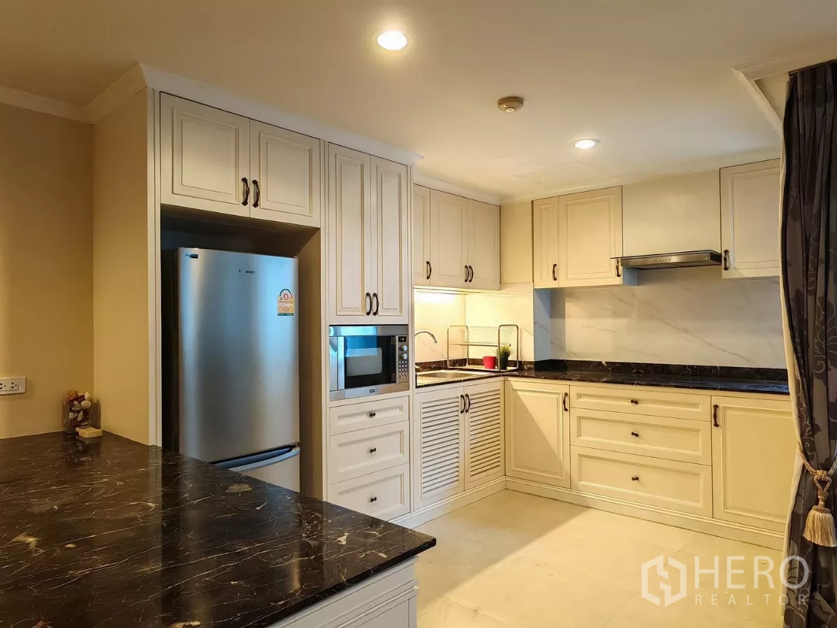 Condominium for rent in Pathum Wan, Bangkok - L-shaped kitchen with range hood, cream cabinetry and marble worktops.