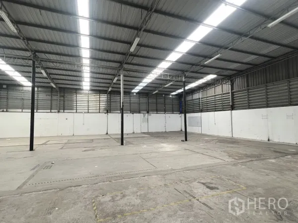 Warehouse for rent in Suan Luang, Bangkok - Open-plan storage space with concrete floor, steel columns, and bright strip lighting.