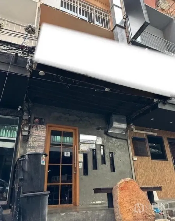 Shophouse for rent or sale in Watthana, Bangkok - Street‑front shophouse facade with glass door, slim windows, concrete wall and deep black awning ready for signage.