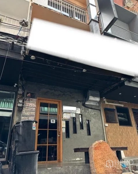 Shophouse for rent or sale in Watthana, Bangkok - Street‑front shophouse facade with glass door, slim windows, concrete wall and deep black awning ready for signage.
