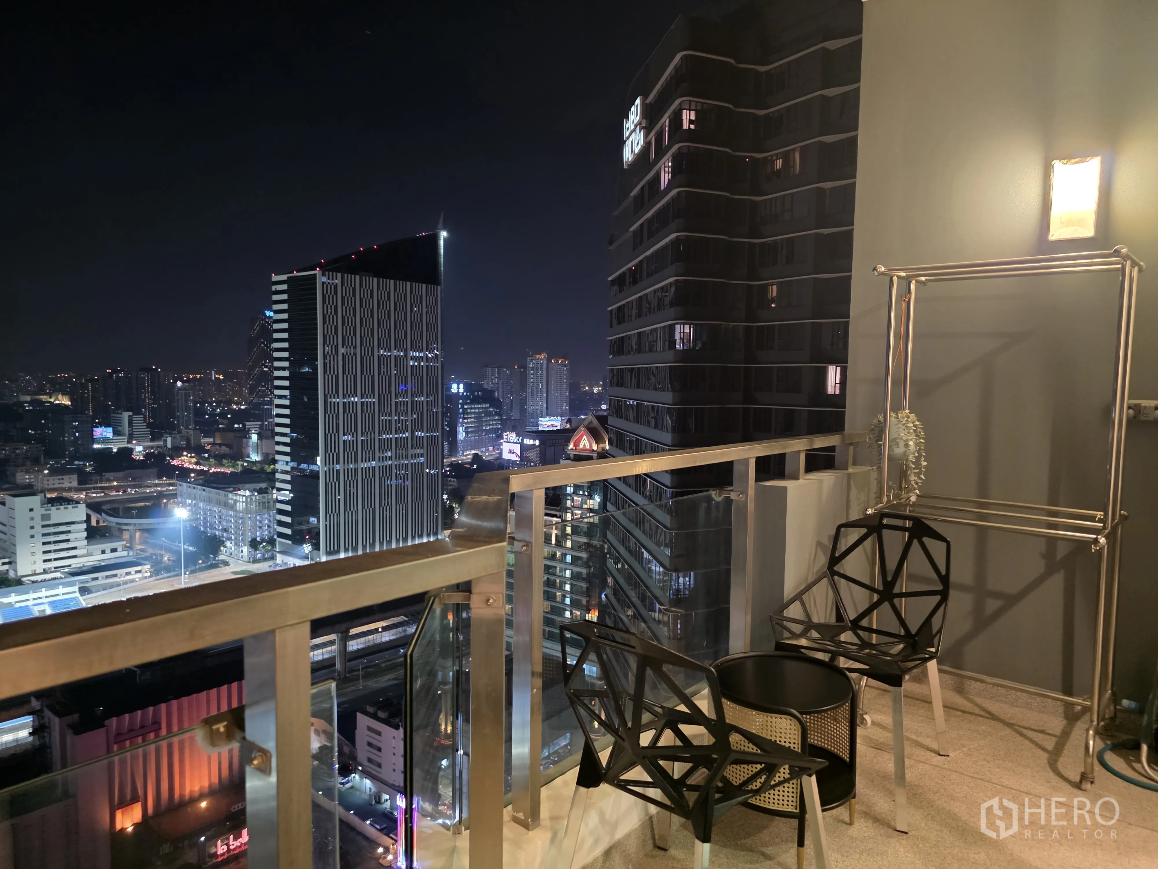 Condominium for rent in Bang Kapi, Bangkok - Balcony seating with two chairs and a small table overlooking city buildings.