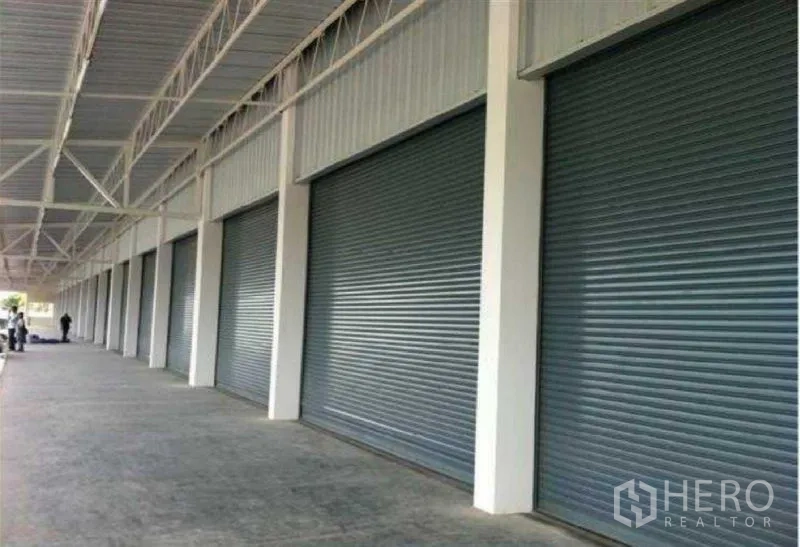 Warehouse for rent in Bang Phli, Samut Prakan - Row of metal roller shutter doors beneath a covered loading area.