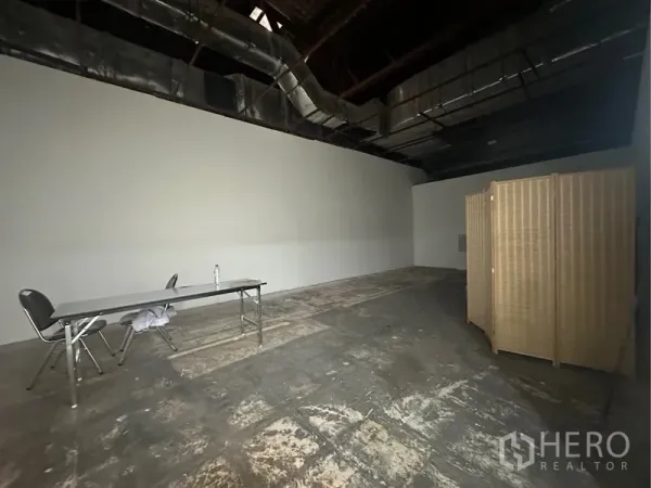 Retail Space for rent - Angle of the shop floor with folding screen divider, concrete-look floor and white walls.