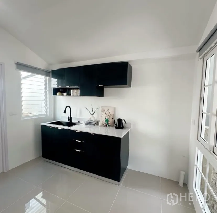 Detached House for rent in Mueang Samut Prakan, Samut Prakan - Fitted kitchen with black cabinetry, white countertop, sink and window.