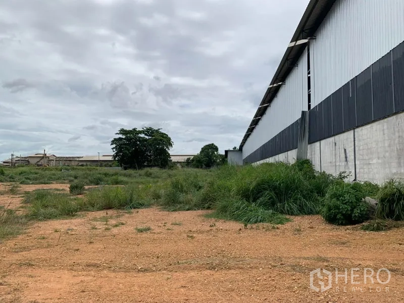 Factory for rent in Chon Buri - Open plot along the factory wall with gravel and grass, ideal for truck staging or future expansion.