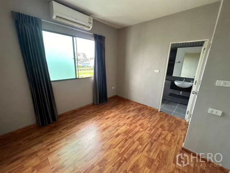 Townhouse for rent or sale in Phra Khanong, Bangkok - Bedroom with wood flooring, window air conditioner, and door to ensuite.
