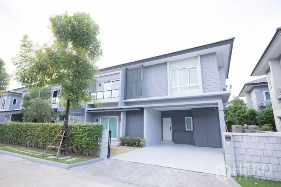 Detached House for sale in Prawet, Bangkok - Street view of a contemporary detached house with green hedge and tiled driveway.