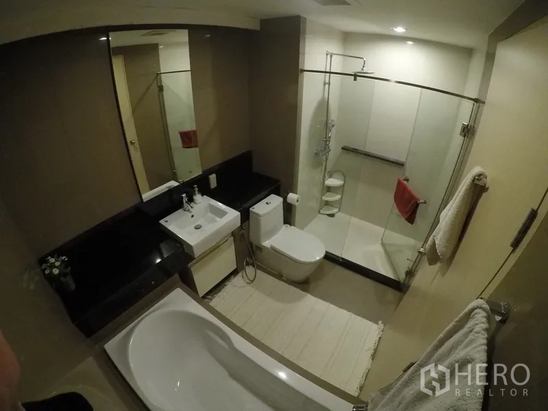Condominium for rent or sale in Khlong Toei, Bangkok - Modern bathroom with bathtub, glass-enclosed shower, vanity and black countertop.