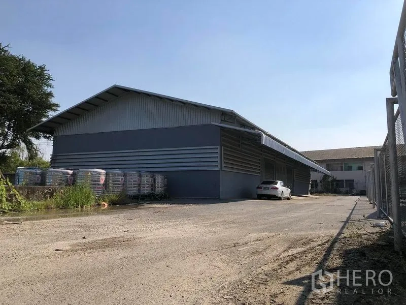 Factory for rent in Bang Bua Thong, Nonthaburi - Wide exterior perspective of the factory with driveway and fenced boundary.
