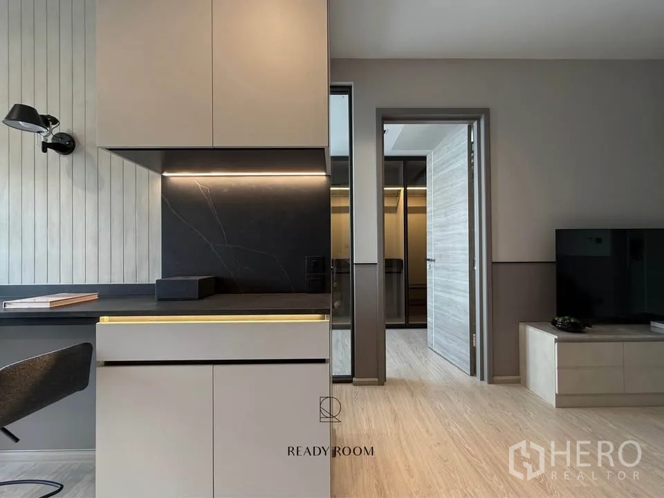 Condominium for rent in Khlong Toei, Bangkok - Sleek kitchen with black stone countertop, under-cabinet lighting, and corridor to bedroom.