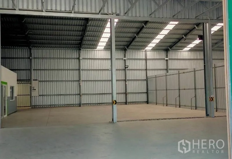 Warehouse for rent in Pak Kret, Nonthaburi - Open loading bay under a high roof with translucent skylights and internal partition fencing.