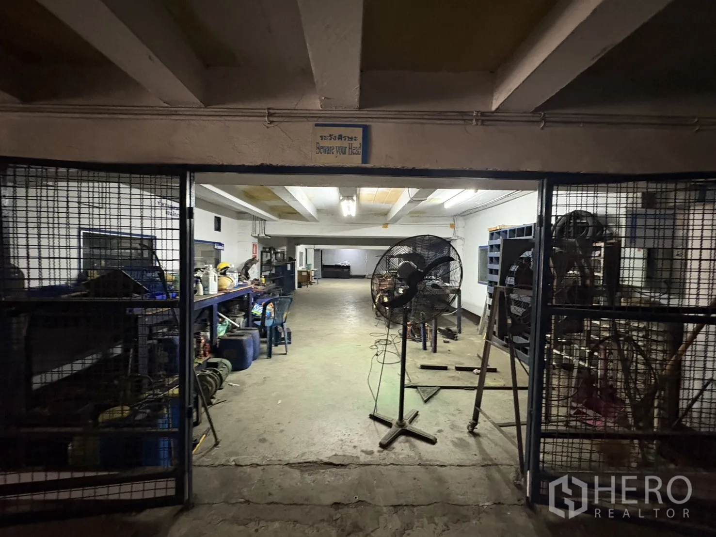 Factory for rent in Phra Pradaeng, Samut Prakan - Basement workshop with caged storage and industrial fans.