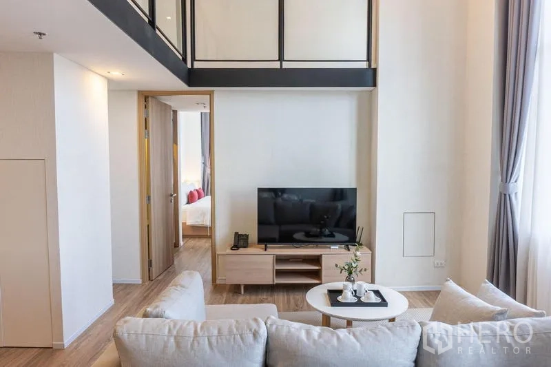 Condominium for rent in Khlong Toei, Bangkok - Cozy living room with TV console and coffee table under a double‑height ceiling next to a bedroom.