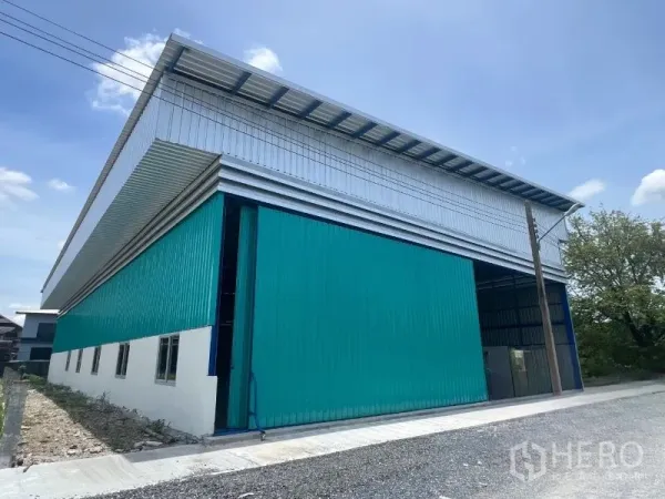 Warehouse for rent in Min Buri, Bangkok - Long side view revealing metal cladding, windows, and a concrete driveway along the building.