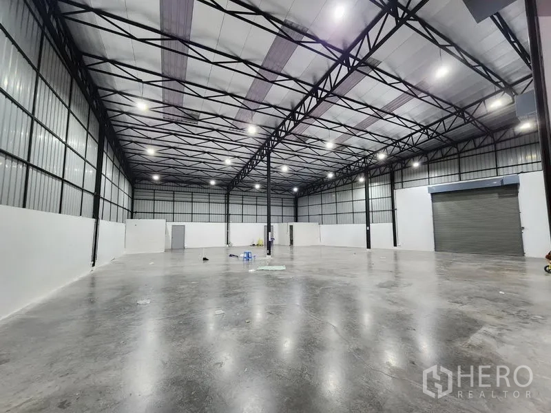 货栈 出租在Pak Kret, Nonthaburi - 大跨距仓储大厅，保温屋顶板、白色墙体及卷闸门入口。