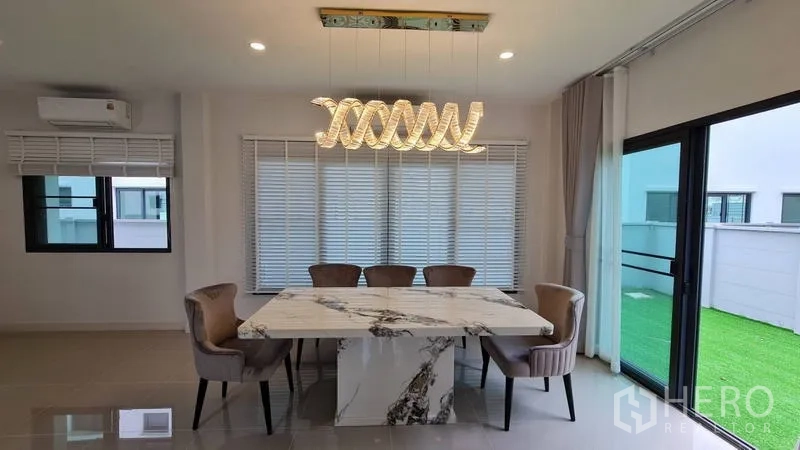 Detached House for rent in Samut Prakan - Dining space with marble-top table and modern pendant lighting by sliding doors.