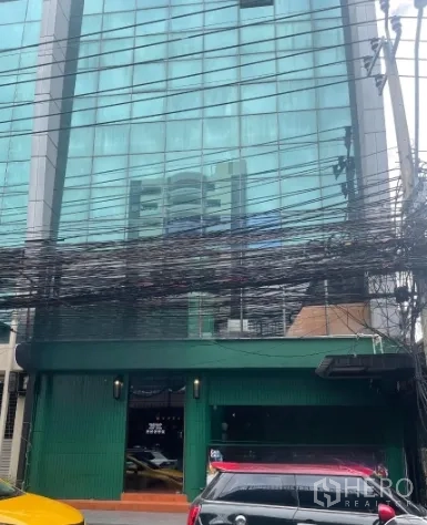 Shophouse for rent in Watthana, Bangkok - Glass-front mixed-use building with green shophouse facade on a city street in Thonglor.
