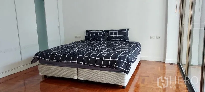 Townhouse for rent in Sathon, Bangkok - Sunlit bedroom with king bed, glossy wood floor and built-in wardrobes beside a balcony.