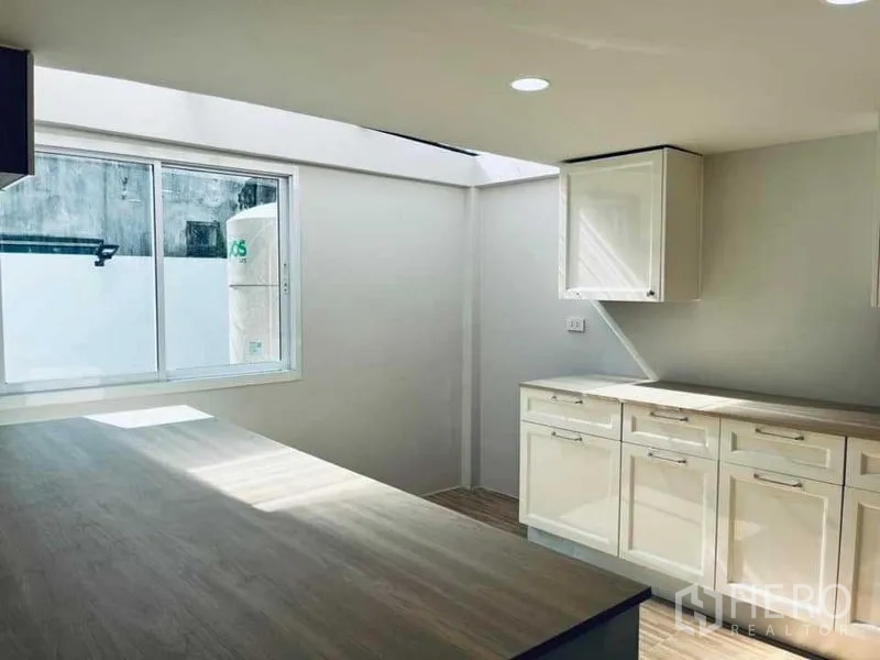 Townhouse for sale in Phra Khanong, Bangkok - Kitchen with skylight, large worktops and glossy storage next to a sliding window.