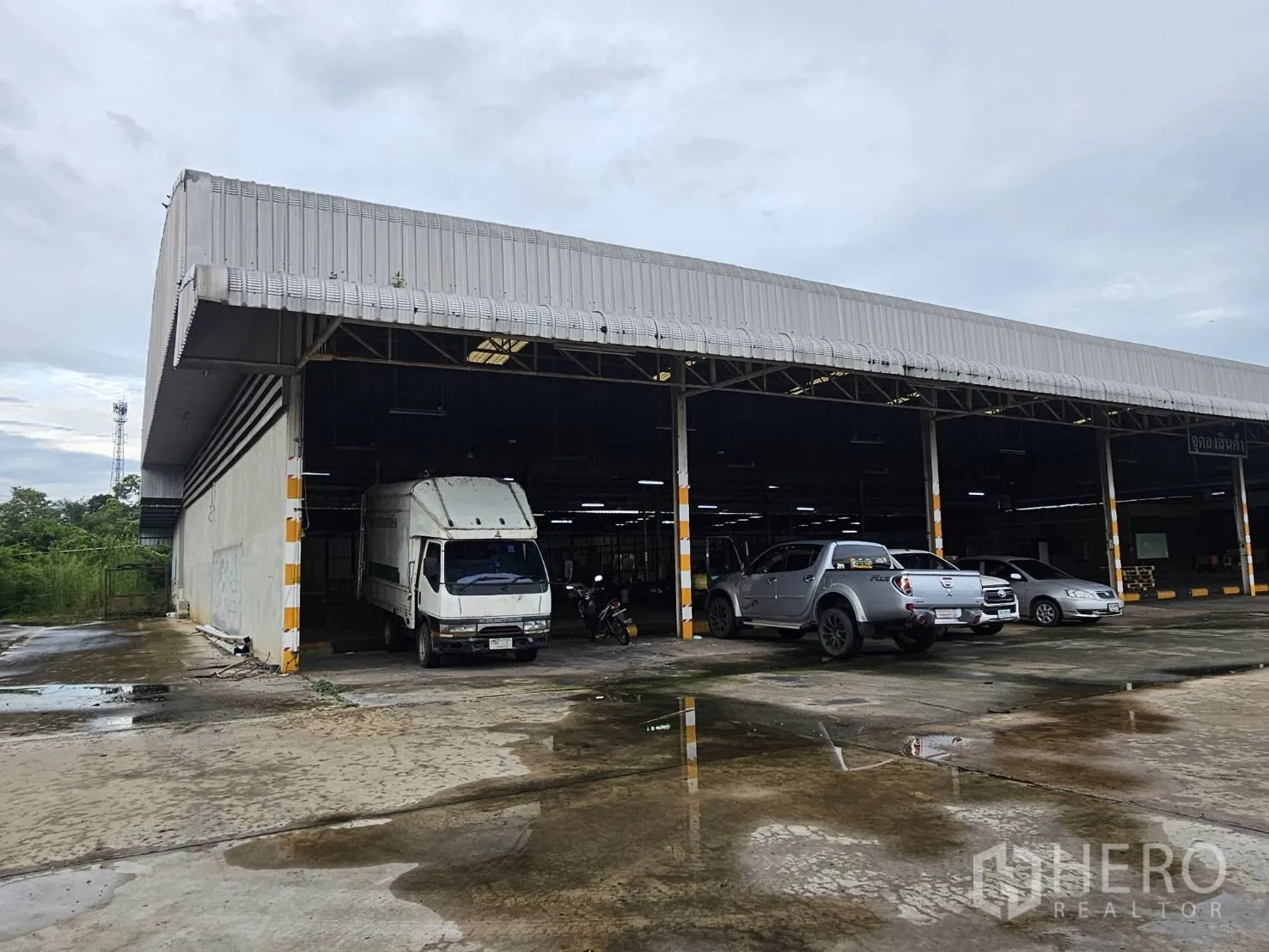 Warehouse for rent in Lam Luk Ka, Pathum Thani - Corner view of covered loading bays with vehicles on wet concrete yard.