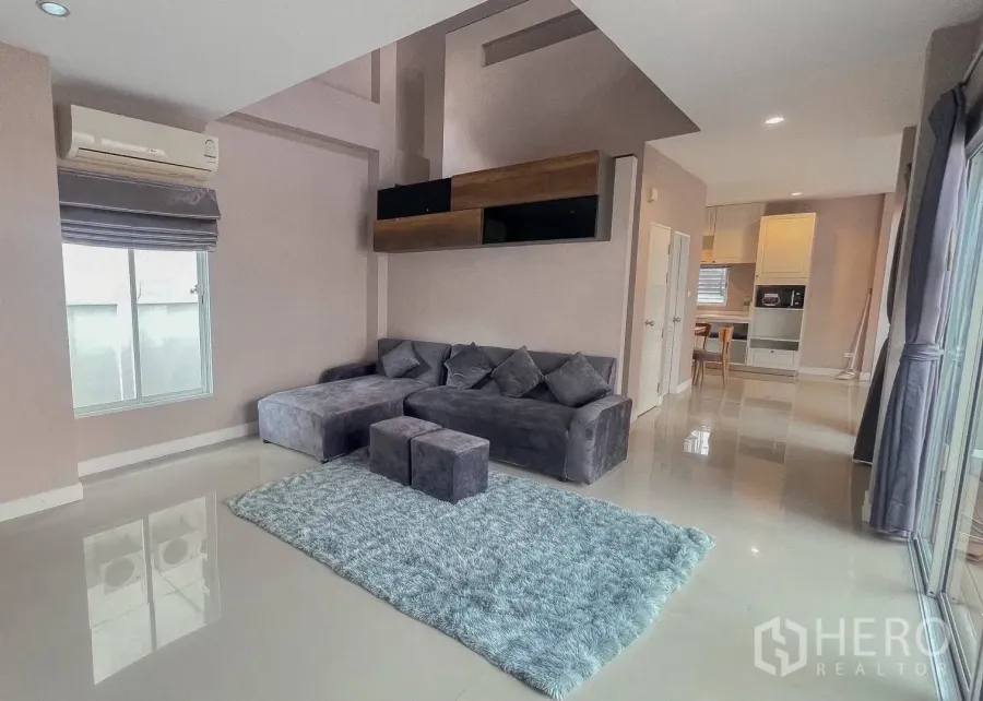 Detached House for rent or sale in Saphan Sung, Bangkok - Living room with gray sectional sofa, rug and sliding glass doors.