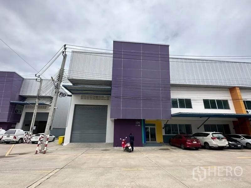 Factory for rent in Bang Phli, Samut Prakan - Front elevation of the unit with purple feature tower, roll‑up gate and covered parking.