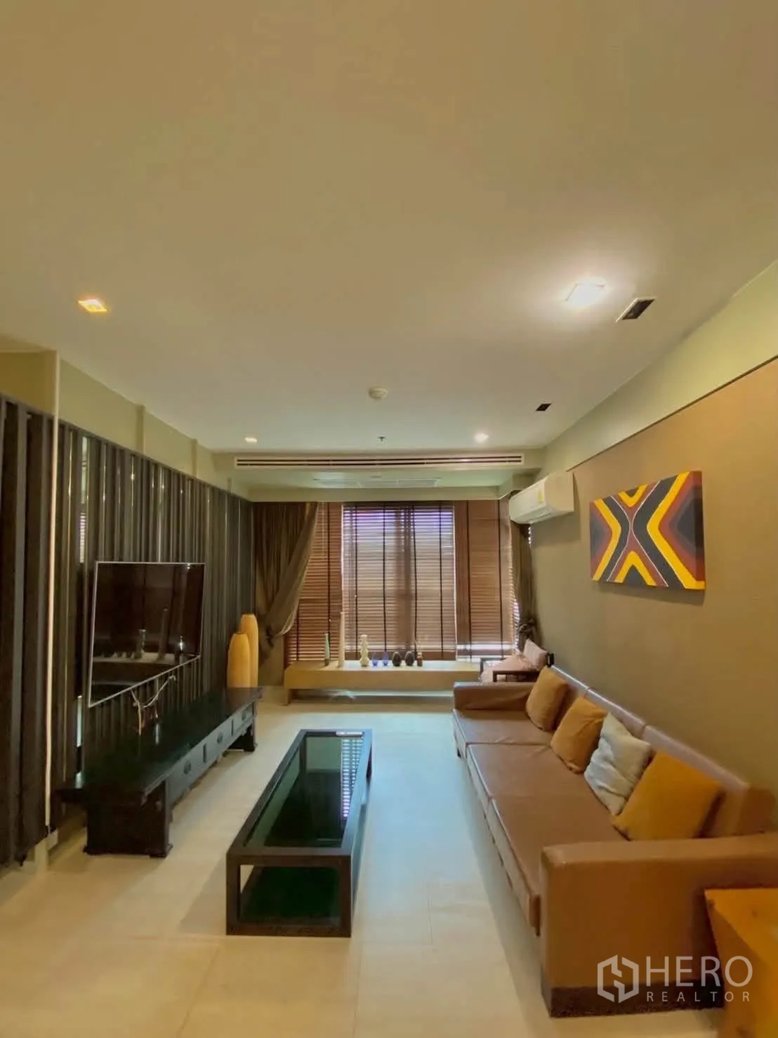 คอนโด for rent in Khlong Toei, Bangkok - ห้องนั่งเล่นพร้อมโซฟาสีน้ำตาล ทีวีติดผนัง และมู่ลี่ไม้
