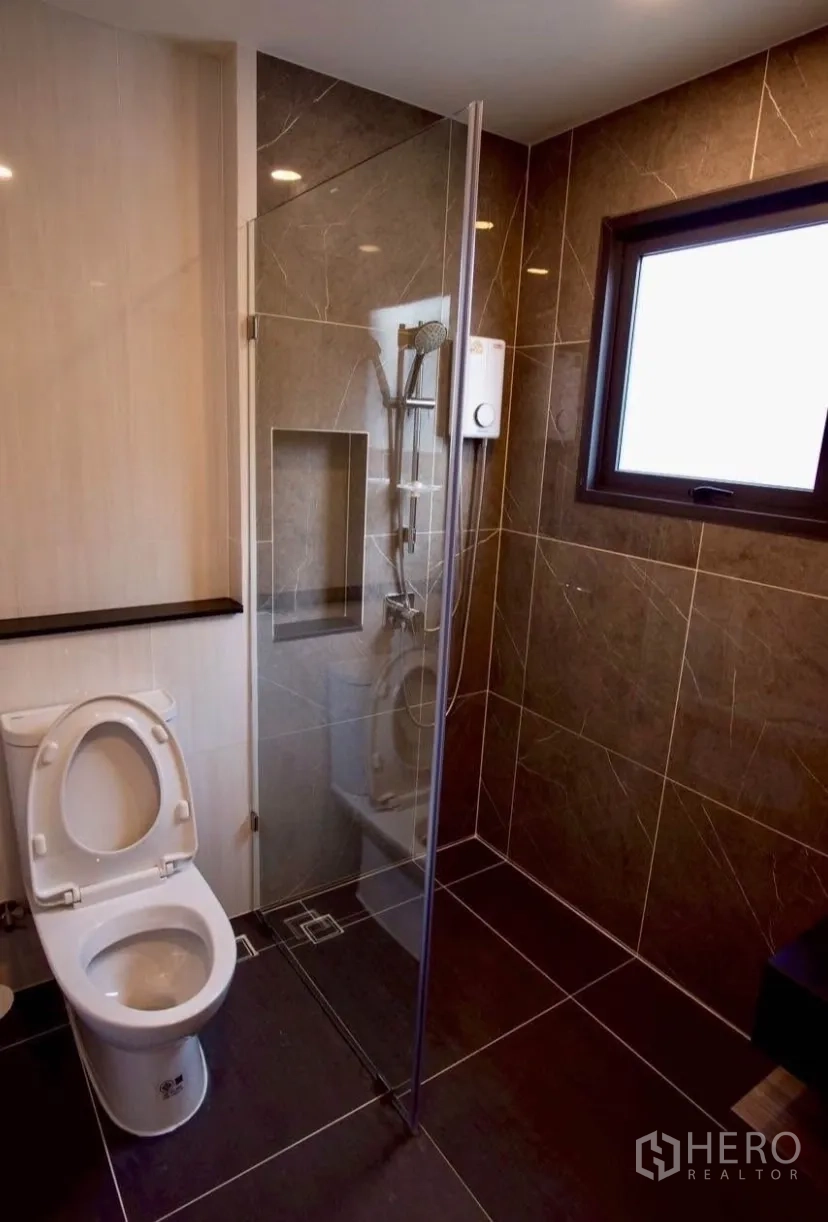 Detached House for rent in Bang Phli, Samut Prakan - Bathroom with glass shower enclosure, dark wall tiles and window.
