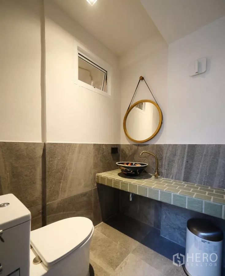 Townhouse for rent or sale in Watthana, Bangkok - Stylish powder room with round mirror, vessel sink and brass faucet.