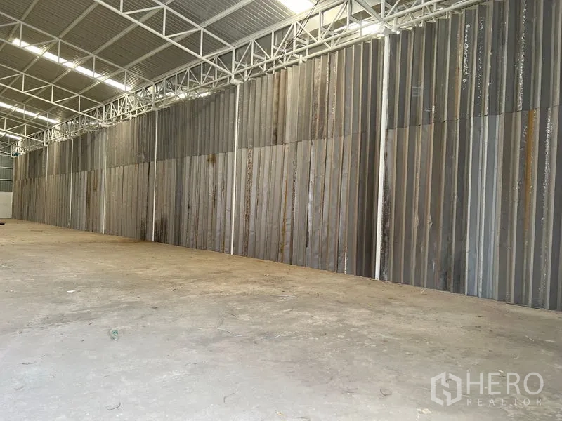 Warehouse for rent in Min Buri, Bangkok - Spacious warehouse interior with concrete floor, high steel trusses and corrugated metal wall.