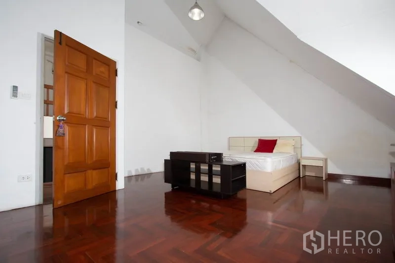 Townhouse for rent in Khlong Toei, Bangkok - Bedroom with sloped ceiling, wooden floor, bed and side tables.