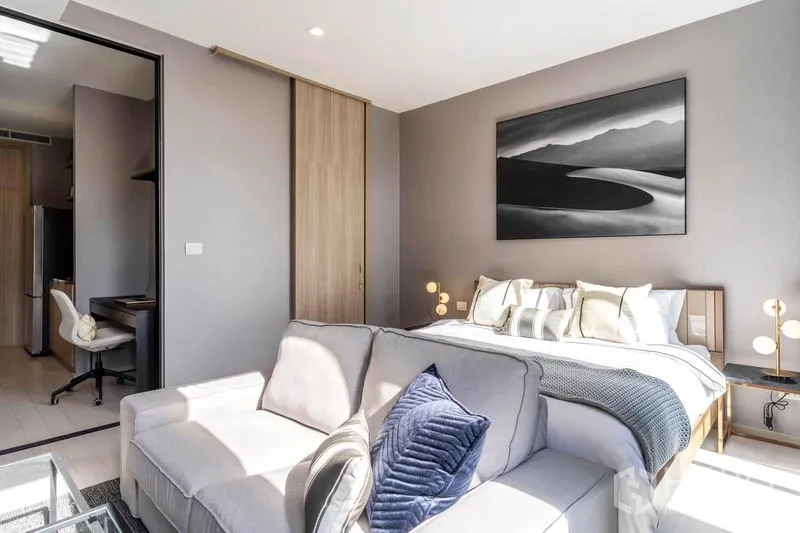 Condominium for rent in Pathum Wan, Bangkok - Bedroom suite with a sofa at the foot of the bed, wall art and warm bedside lighting.