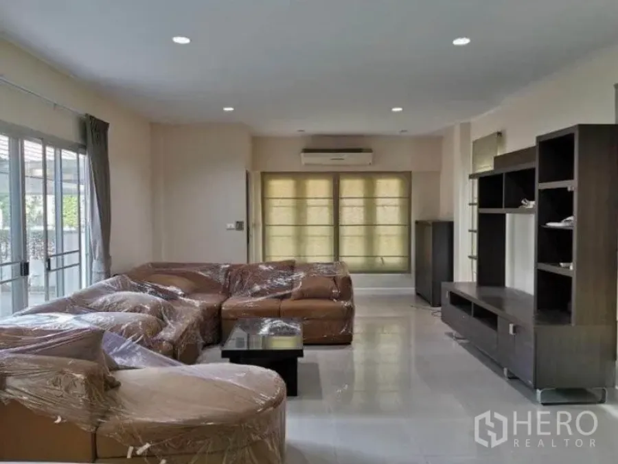 Detached House for rent in Bang Kapi, Bangkok - Bright living room of detached house in Bang Kapi with L‑shaped sofa, TV cabinet, sliding windows and tiled floor.
